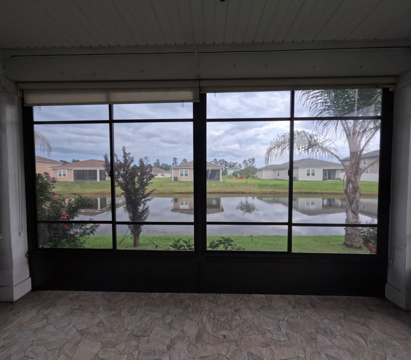 Enclosed porch with dark-framed vinyl windows looking out over a neighborhood pond
