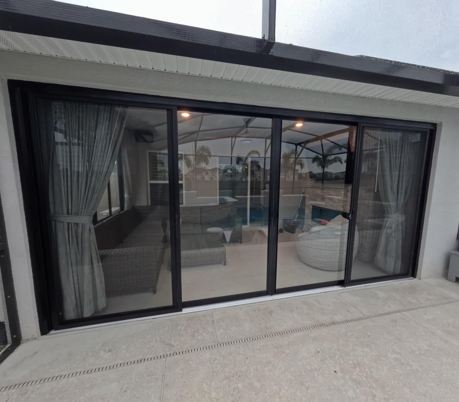 Black-framed sliding vinyl panel enclosure on a covered lanai inside a pool cage
