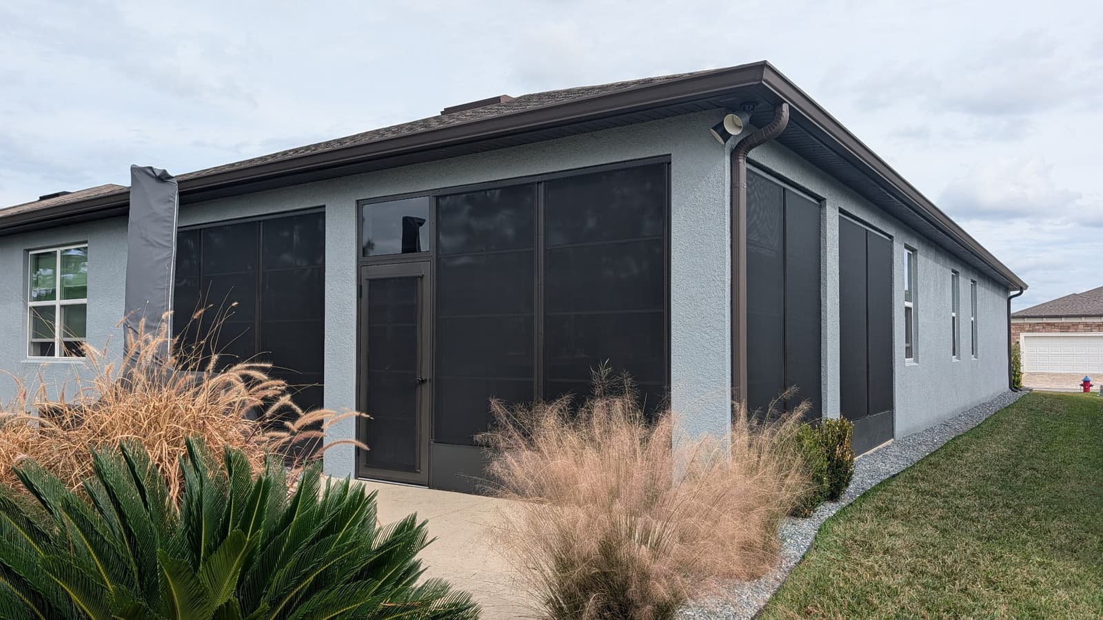 Gray stucco home with a porch enclosed in dark bronze vinyl windows and solar shades